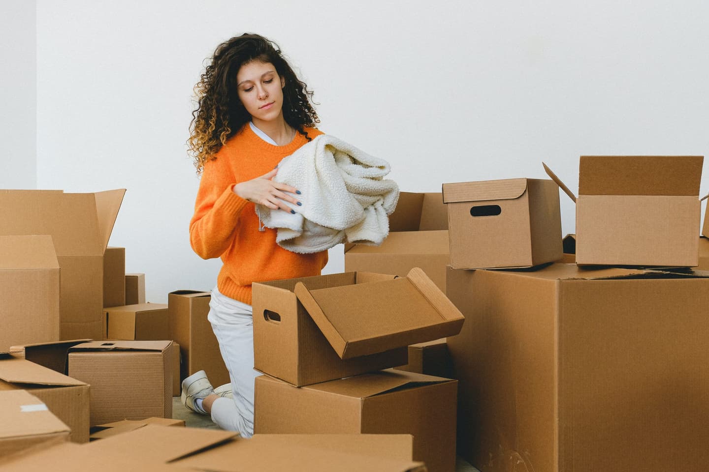 Vrouw tilt een verhuisdoos op tussen niet-uitgepakte dozen in een woonkamer